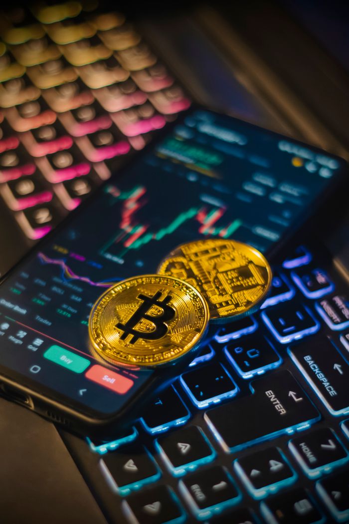 gallery-1 Teclado colorido junto a monedas de Bitcoin y una pantalla de trading para el análisis de criptomonedas.